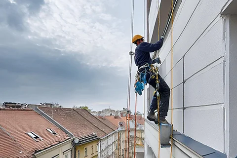 covek farba fasadu na alpinističkim konopcima