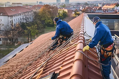 dve osobe su na vrhu krova, osigurane konopcima za radove na visini