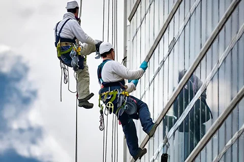dve osobe vise na alpinističkim konopcima i peru prozore na zgradi
